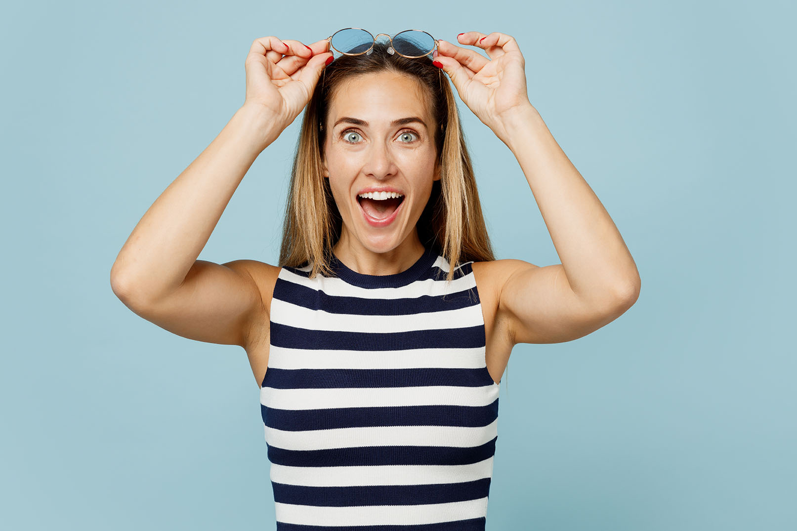 Young surprised fun blonde beautiful woman wear striped tank shirt casual clothes take off sunglasses look camera isolated on plain pastel light blue cyan background studio portrait. Lifestyle concept